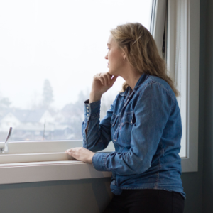 Kvinna som står och tittar ut genom fönstret