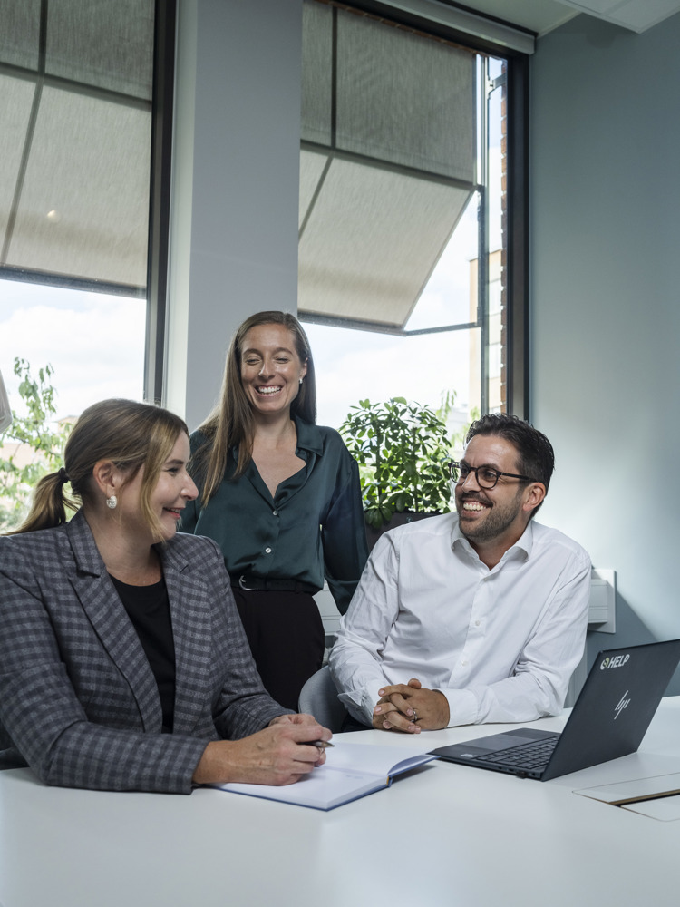 Två kvinnor och en man som sitter i möte och skrattar
